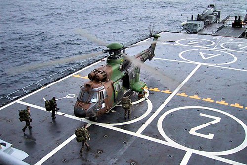 Sur le pont du navire, des commandos embarquent à bord d'un hélicoptère Cougar de l'ALAT