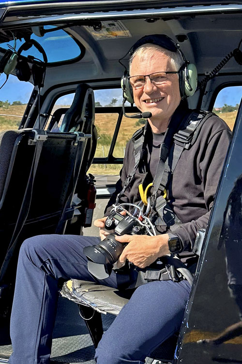 André BOUR avec le harnais en place arrière de l'hélicoptère dans la position de prise des photos porte-ouverte